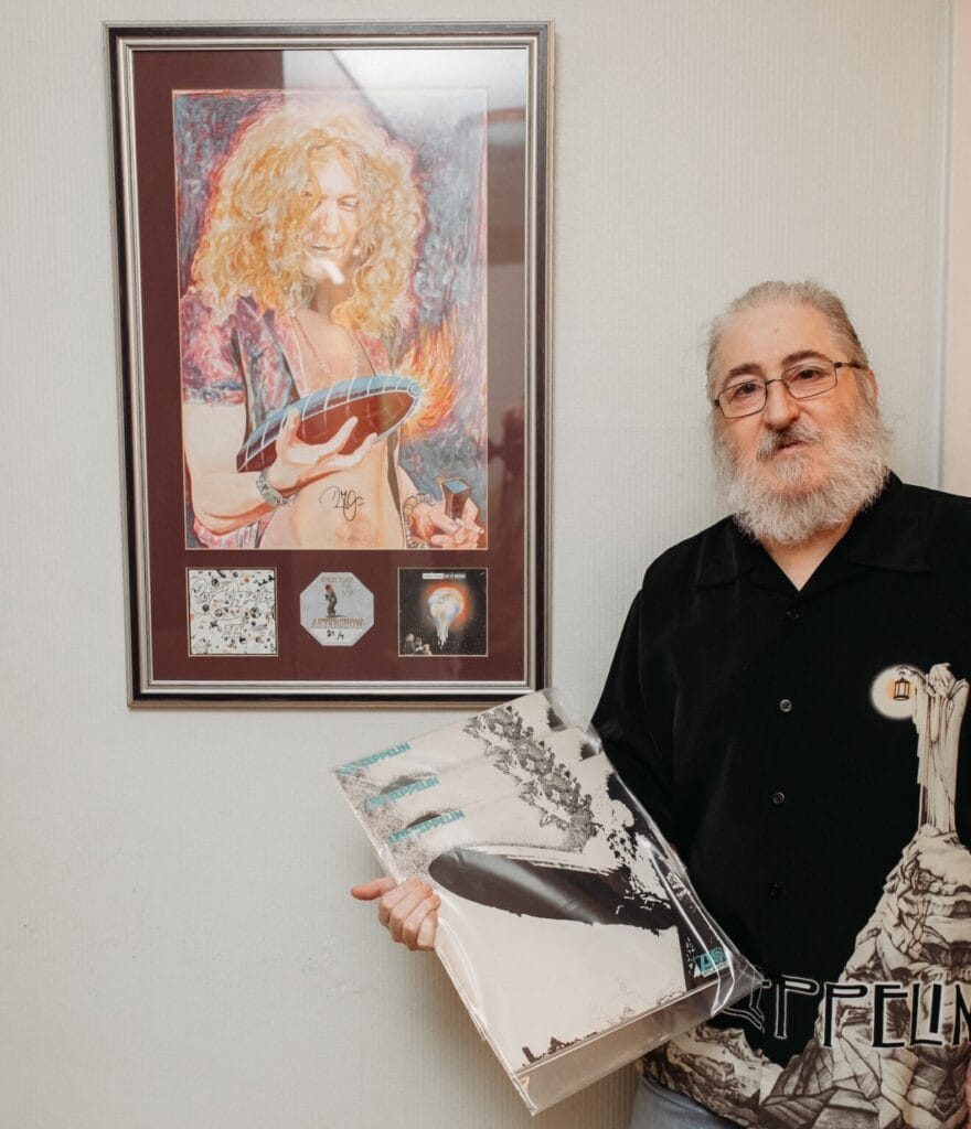 Oleg Korsunskiy segura três cópias antigas do álbum de estreia do Led Zeppelin, com capa turquesa, em frente a um retrato de Robert Plant autografado 